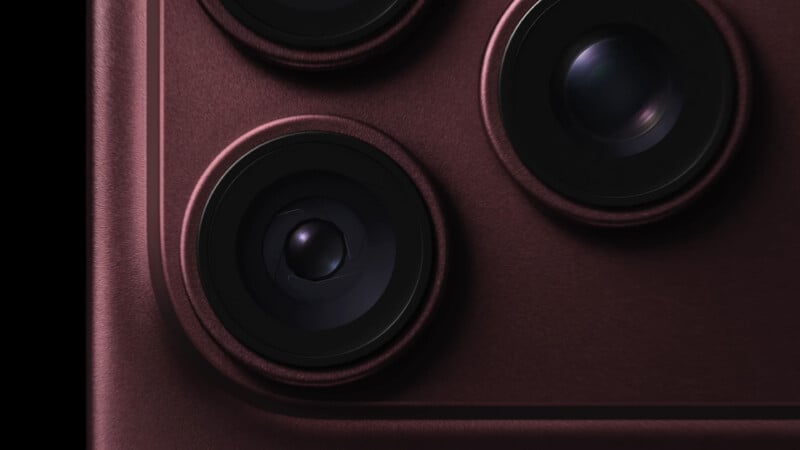 A close-up view of a smartphone camera module featuring three circular lenses set into a dark, textured, maroon-colored housing.