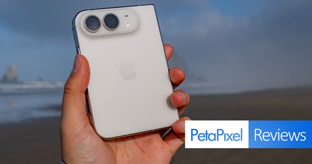 A hand holds a white smartphone with a dual-camera module on the back, with a PetaPixel Reviews logo in the corner.