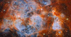 A vibrant nebula filled with swirling clouds of orange dust and glowing blue gas, dotted with numerous bright, sparkling stars.