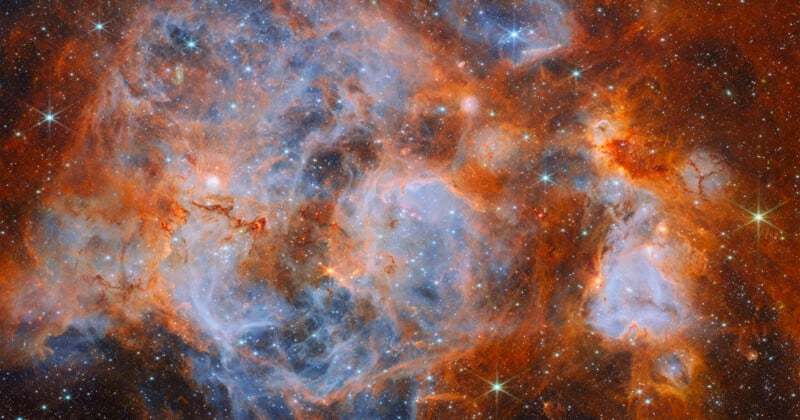 A vibrant nebula filled with swirling clouds of orange dust and glowing blue gas, dotted with numerous bright, sparkling stars.
