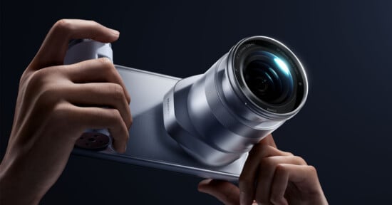 A pair of hands holds a silver smartphone with a large, protruding camera lens attachment on the back, featuring the text "HUAWEI" and "XMAGE" printed on the device.