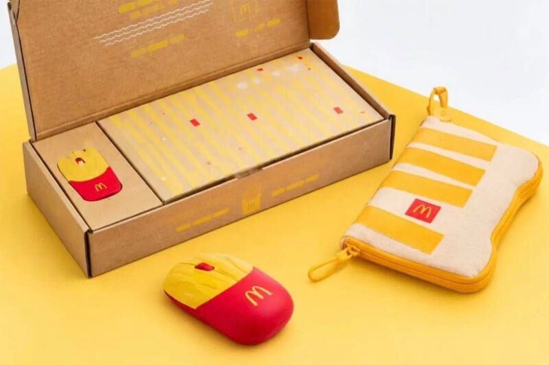 A McDonald's-themed computer mouse shaped like a box of fries sits next to its open cardboard packaging and a matching yellow and white striped zippered pouch.