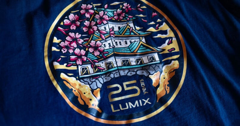 A circular graphic on a dark blue fabric featuring a Japanese-style castle surrounded by cherry blossoms, with the text "25 years LUMIX" printed below.
