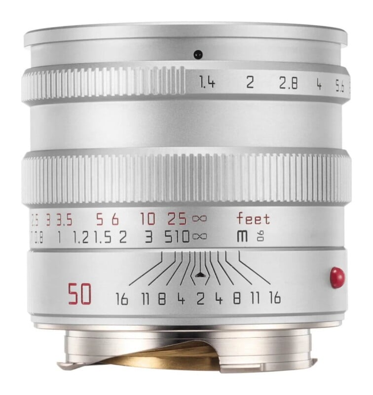 A silver camera lens with a manual focus ring, aperture ring, and depth-of-field scale, featuring markings in feet and meters.