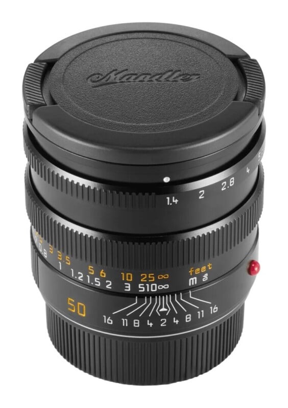 A black camera lens with a lens cap labeled "Mandler" stands upright, showing aperture markings from 1.4 to 16 and a distance scale in feet and meters.