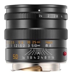 A black manual focus camera lens with aperture and distance markings, featuring a red dot on the side and a metal mount.