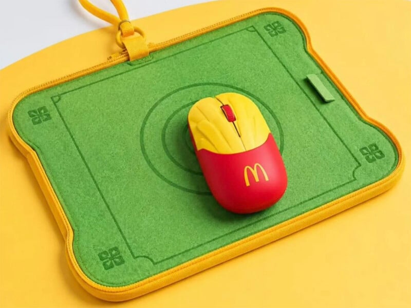 A McDonald's-themed computer mouse shaped like a carton of french fries sits on a green, rectangular felt mousepad with a yellow border and a yellow strap.