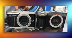Two digital cameras sit side-by-side on a surface, with the left one labeled "OLYMPUS PEN" and the right one labeled "NBD" and "G500".
