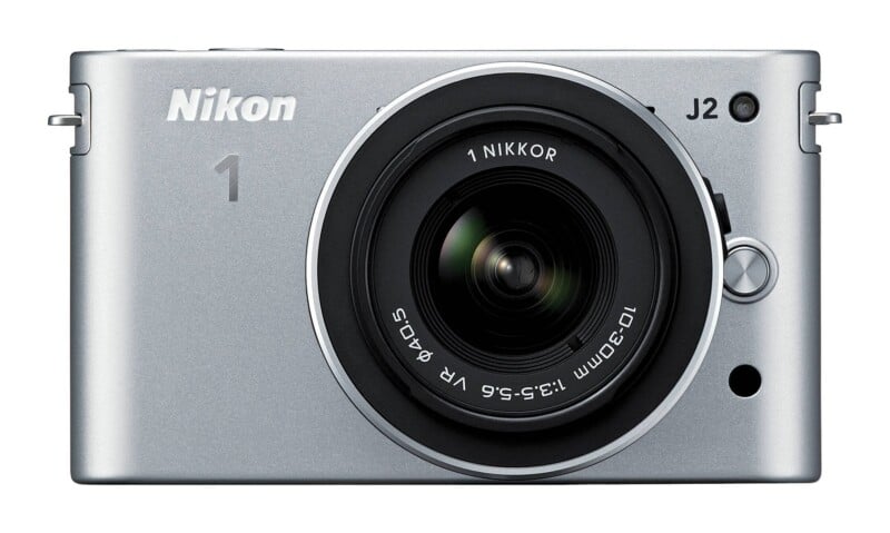 A silver Nikon 1 J2 mirrorless camera with a 1 NIKKOR 10-30mm lens attached, viewed from the front.