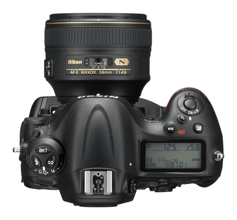 Top-down view of a black Nikon DSLR camera with an attached 58mm lens, showing the top LCD screen, shutter button, and various control dials.