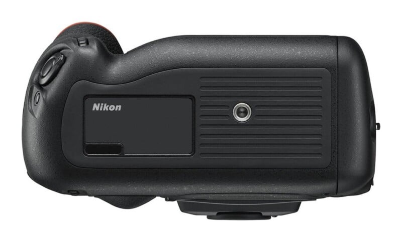 A bottom view of a black camera body showing a tripod mount socket, a rubberized grip area, and a Nikon logo.