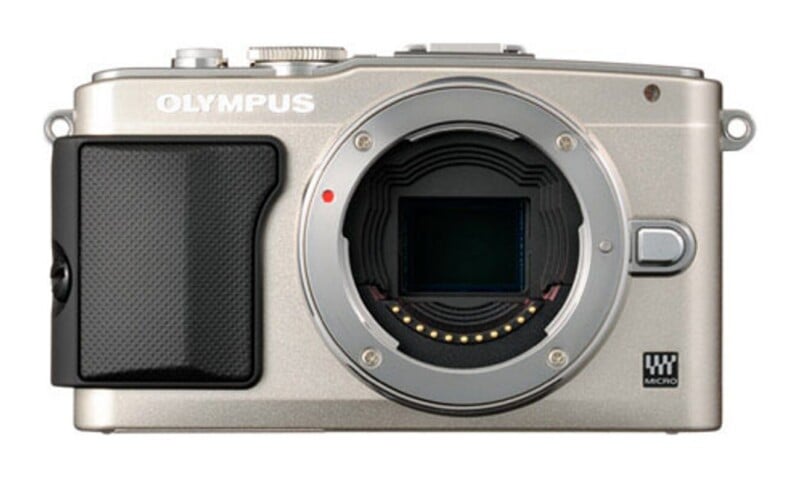 A silver Olympus mirrorless camera body shown from the front with the lens removed, revealing the sensor and lens mount.