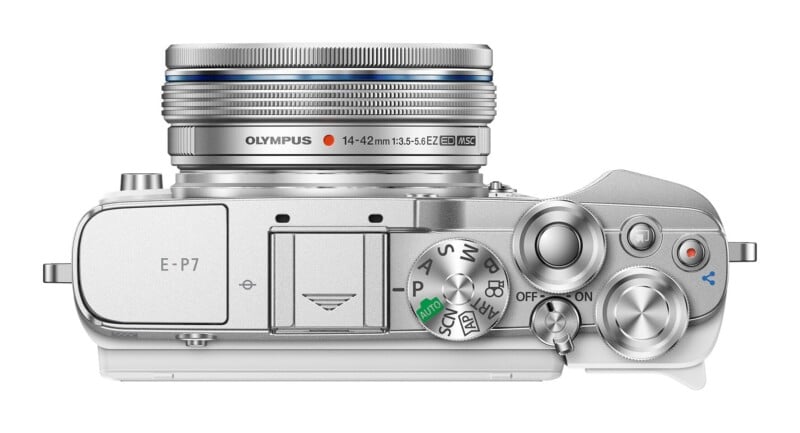 Top-down view of a silver Olympus E-P7 camera body with a 14-42mm lens attached, showing the mode dial, shutter button, and power switch.