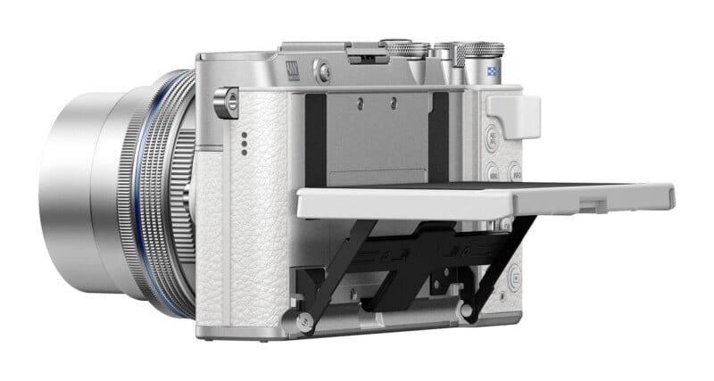 A silver mirrorless camera with a white textured grip and a rear LCD screen tilted downward on a hinged bracket.