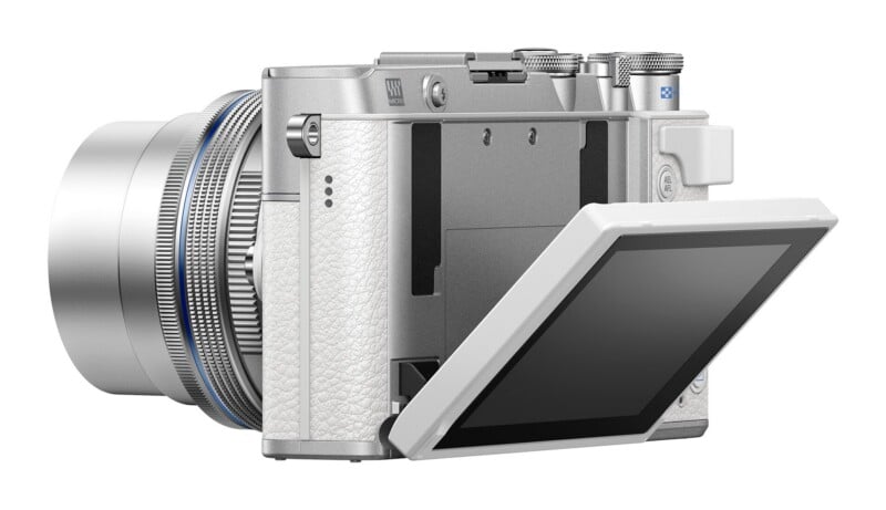 A silver mirrorless camera with a white textured grip and a rear screen tilted outward, viewed from the back-left angle.