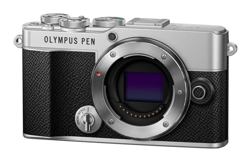 A silver and black Olympus Pen mirrorless camera body shown from the front, featuring a lens mount, a color/mono switch, and textured grip.
