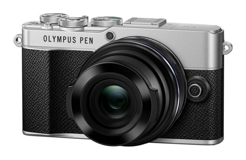 A silver and black Olympus Pen E-P7 mirrorless camera with a black lens attached, viewed from the front against a white background.