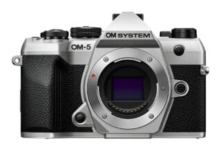 A silver and black OM SYSTEM OM-5 mirrorless camera body viewed from the front, showing the lens mount and sensor.