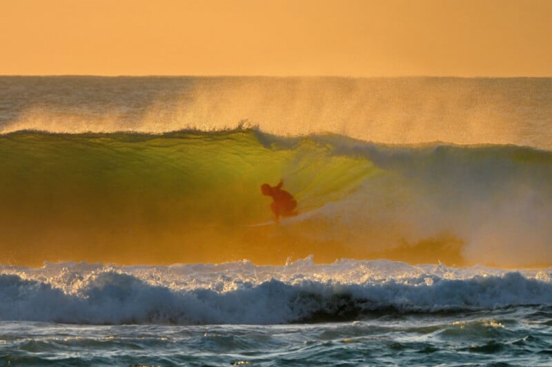 A surfer rides inside the barrel of a golden, sunlit wave at sunset.
