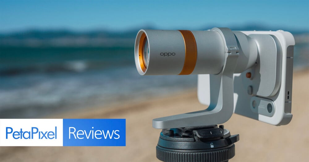 A silver Oppo-branded camera lens attachment mounted to a smartphone on a tripod, with a beach and ocean in the background.