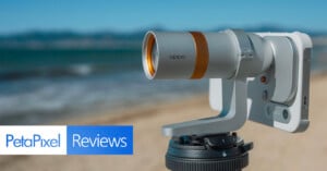 A silver Oppo-branded camera lens attachment mounted to a smartphone on a tripod, with a beach and ocean in the background.