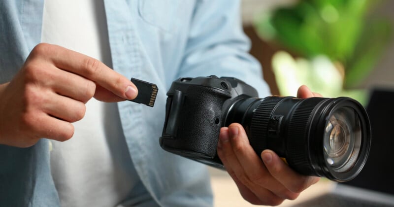 A person in a light blue shirt holds a black camera in one hand and an SD memory card in the other.