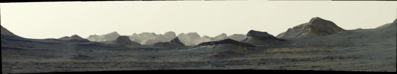 A wide, panoramic view of a barren, rocky Martian landscape with layered hills and distant mountains under a pale, hazy sky.
