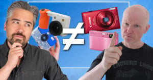 Two men stand on either side of a large not-equal sign, with the man on the left holding a toy-like camera and the man on the right gesturing toward a red Canon and a pink Sony camera.