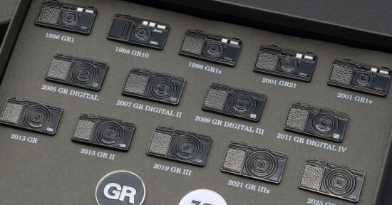 A collection of Ricoh GR camera pins arranged in a grid on a dark gray display board, each labeled with its model name and year.