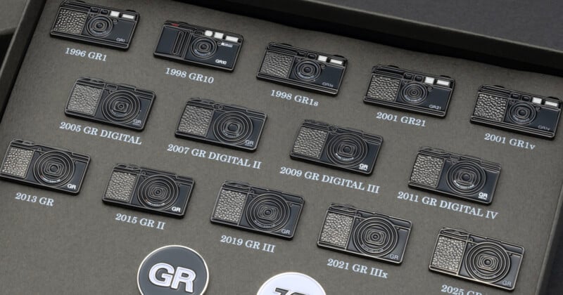 A collection of Ricoh GR camera pins arranged in a grid on a dark gray display board, each labeled with its model name and year.
