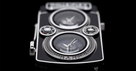 A close-up of a black and silver watch designed to resemble a vintage twin-lens reflex camera, featuring two circular clock faces and the text "FRANKE & HEIDECKE GERMANY" on the lower lens area.