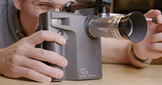 A person looks through the viewfinder of a gray EPixPro camera while holding the lens with their right hand.