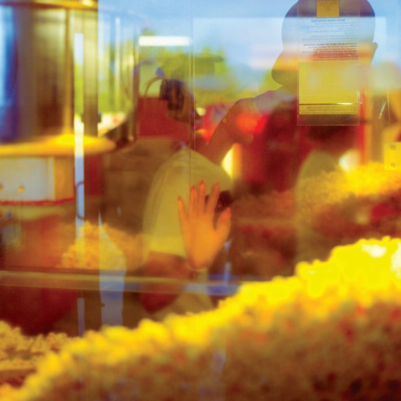 A person's hand is pressed against the glass of a popcorn machine, with their reflection visible in the window.