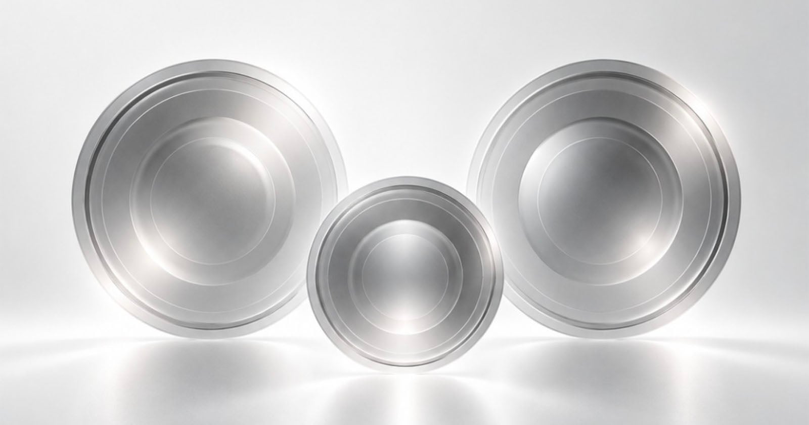Three metallic, circular, bowl-like objects are arranged in a row against a bright, white background.