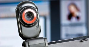 A black webcam with a prominent red ring around the lens is mounted on top of a computer monitor.
