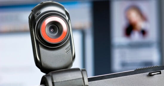 A black webcam with a prominent red ring around the lens is mounted on top of a computer monitor.