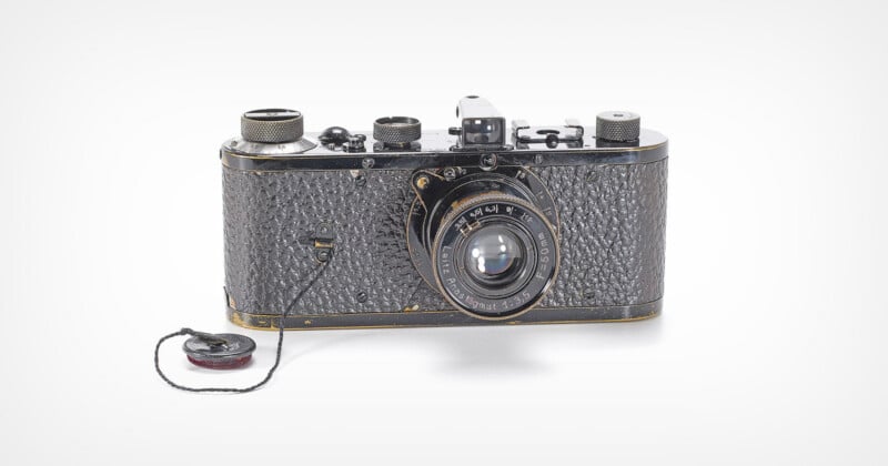 A vintage black film camera with a textured body and a lens labeled "Leitz Anastigmat 1:3,5 F=50mm," featuring a lens cap attached by a string.
