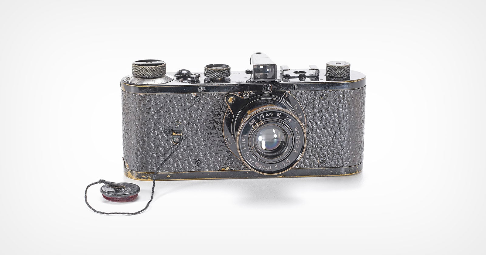 A vintage black film camera with a textured body and a lens labeled "Leitz Anastigmat 1:3,5 F=50mm," featuring a lens cap attached by a string.
